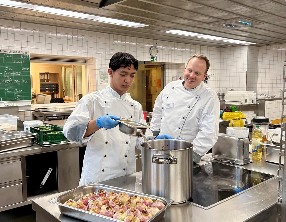 Zwei Personen in Koch-Kleidung am Herd schütten Sud in einen Topf