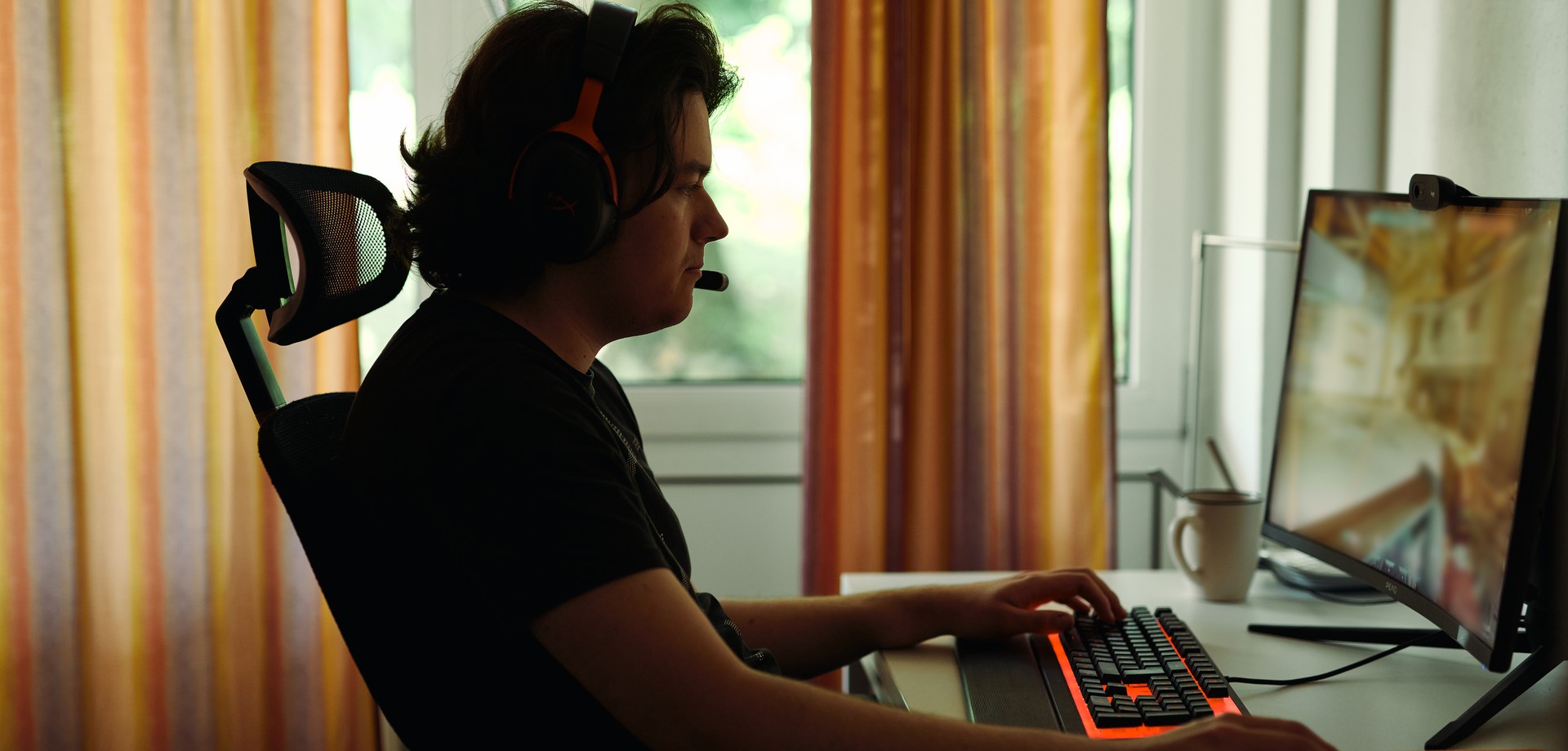 Junger Mann mit Headset spielt an einem PC mit farbig leuchtender Tastatur