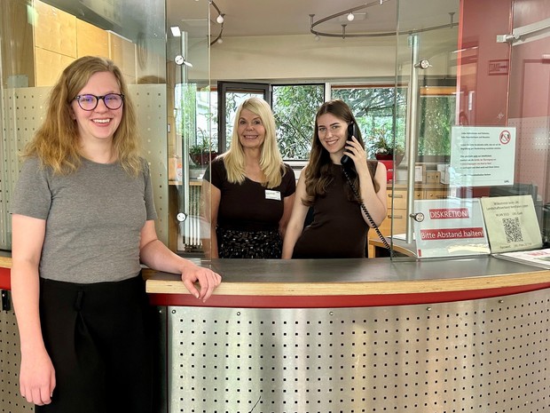 Drei Frauen an einem Empfangstresen. Eine steht davor und zwei dahinter, von denen eine zu telefonieren scheint. Drei Frauen an einem Empfangstresen. Eine steht davor und zwei dahinter, von denen eine zu telefonieren scheint.