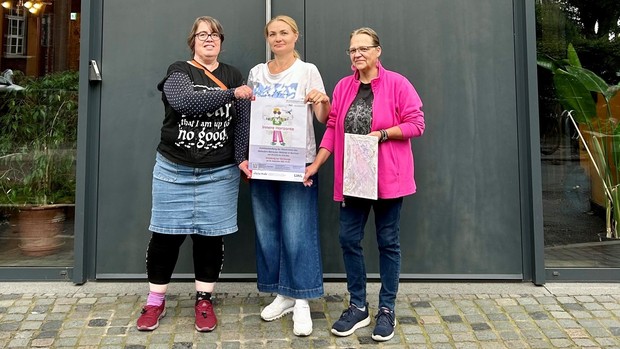 Drei Frauen mit Veranstaltungsplakat vor einer Tür
