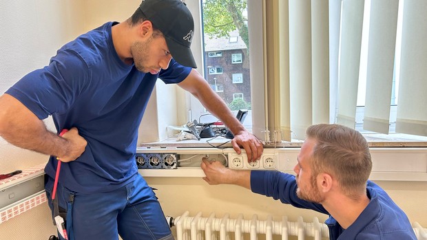 Zwei Männer in Arbeitskleidung arbeiten an einem Kabelkanal.