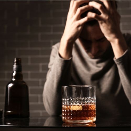 Niedergeschlagener Mann vor alkoholischem Drink und Flasche daneben