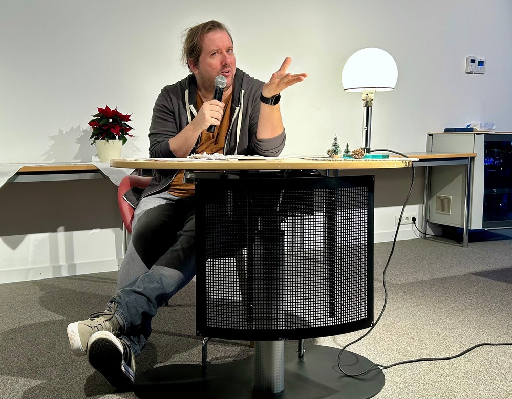 Mann sitz an einem Tisch mit Mikrofon in der Hand liest aus einem Buch