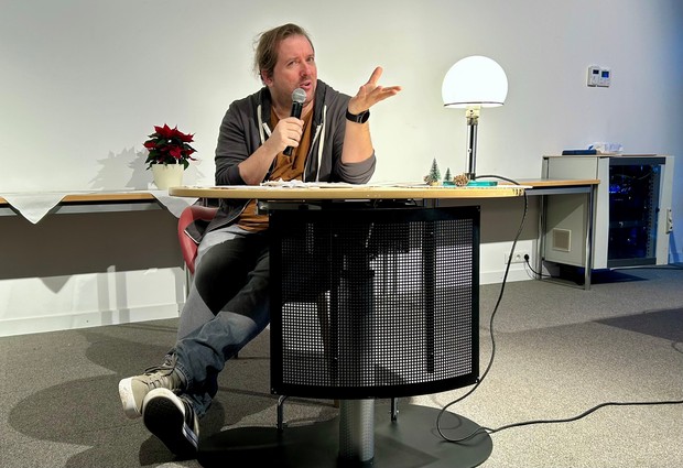 Mann sitz an einem Tisch mit Mikrofon in der Hand liest aus einem Buch