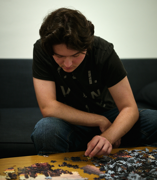 Junger Mann sitzt auf einem Sofa und puzzelt.