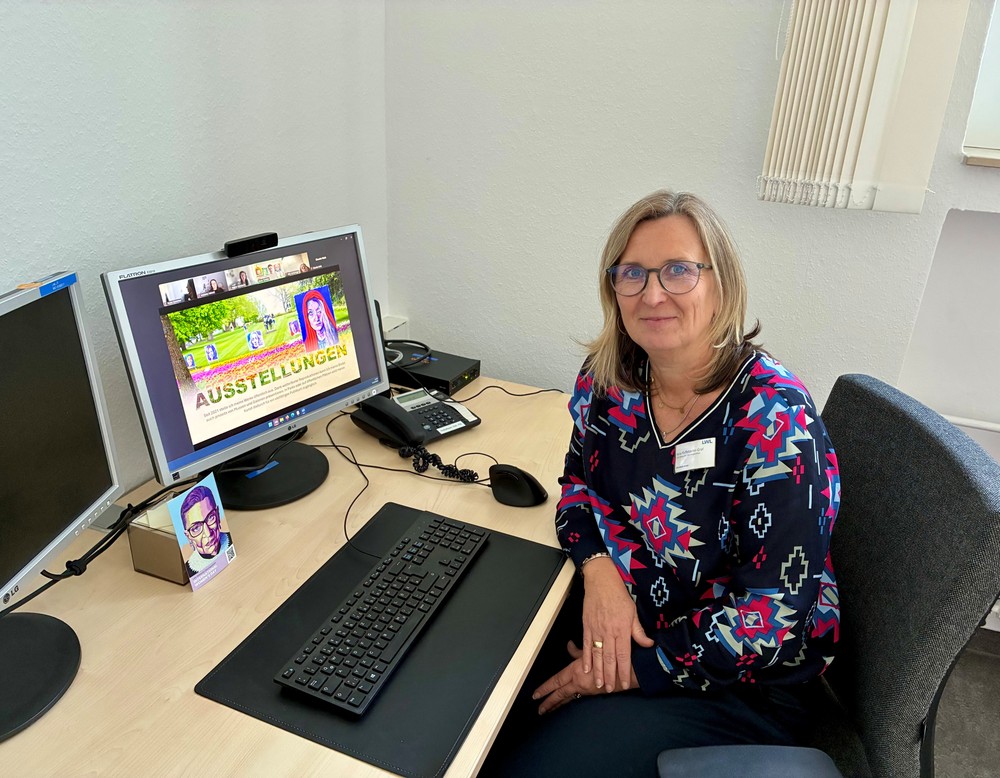 Eine Frau sitzt an einem Schreibtisch vor einem Computer mit geöffneter Präsentation.