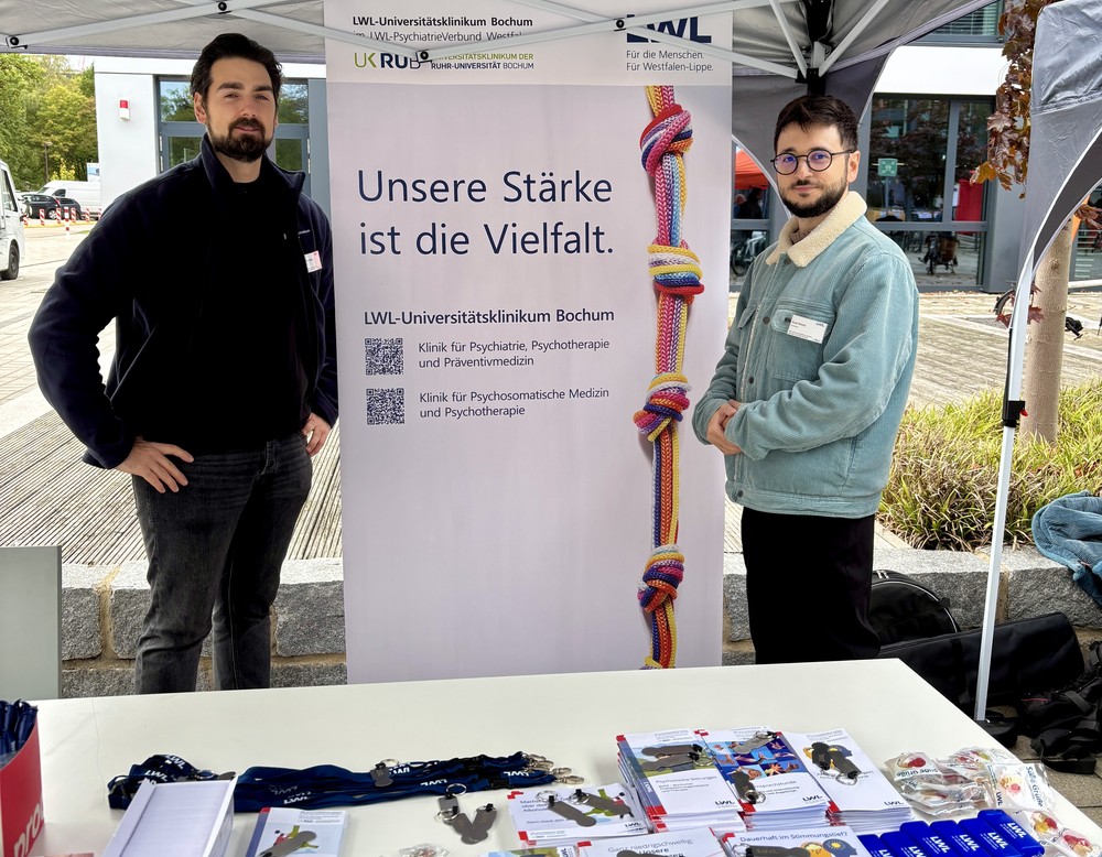 Zwei Mitarbeiter des LWL-Universitätsklinikums Bochum am Infostand mit Broschüren, Flyern und Werbeartikeln.