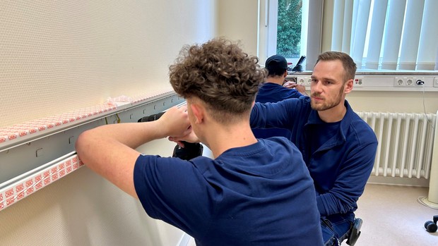 Zwei Männer in Arbeitskleidung arbeiten an einem Kabelkanal.